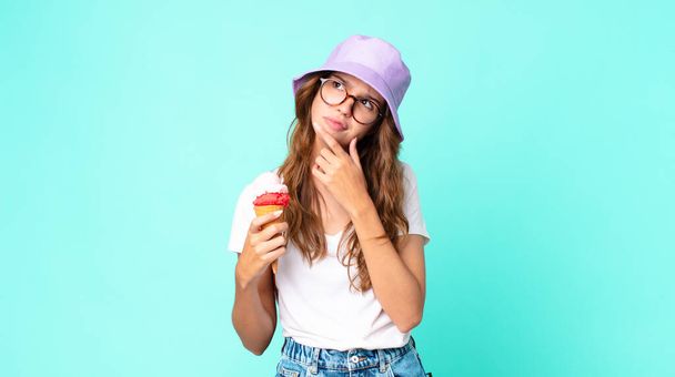 young pretty woman thinking, feeling doubtful and confused holding an ice cream. summer concept - Foto, imagen