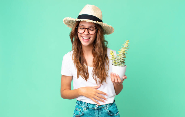 young pretty woman laughing out loud at some hilarious joke with a straw hat and holding a cactus - Фото, зображення