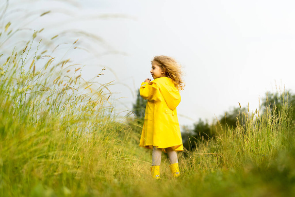 Улыбающаяся блондинка в желтом плаще на природе после дождя, счастливое детство - Фото, изображение