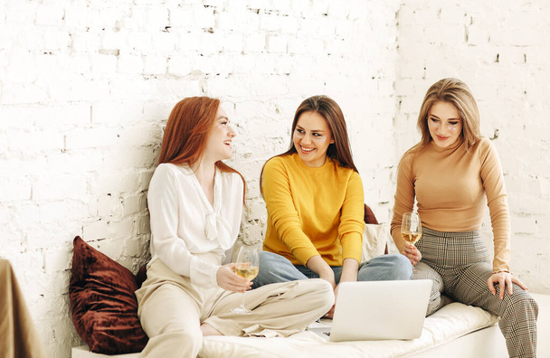 Αισιόδοξες νεαρές γυναίκες χαμογελούν με μπαλώματα στο πρόσωπο ενώ αναπαύονται κοντά σε τραχύ τοίχο βλέποντας ταινία στον υπολογιστή - Φωτογραφία, εικόνα