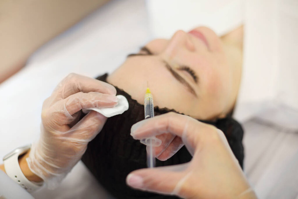 美容クリニックでアンチエイジング手術中に女性の目の近くにヒアルロン酸を注入するプロの美容師 - 写真・画像