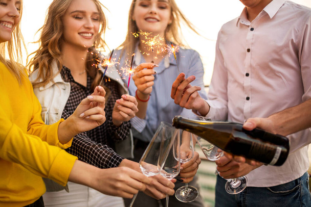 Grupa przyjaciół imprezowanie z fletów z szampanem i bengal ognia zabawy na imprezie na dachu - Zdjęcie, obraz