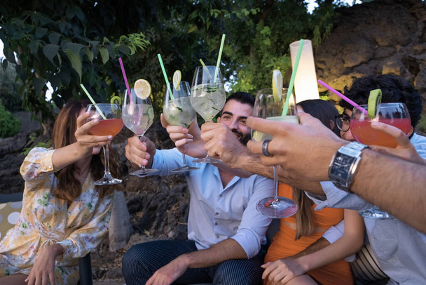 Gruppo di giovani che si riuniscono sul terrazzo giardino per un cocktail party alzando i calici per un brindisi celebrativo. - Foto, immagini