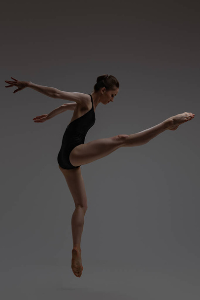 Вид збоку знімок стрибаючої балерини на сірому фоні
 - Фото, зображення