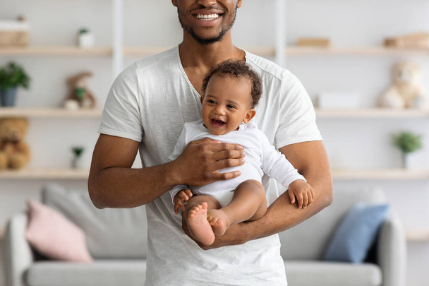 Uśmiechnięty młody czarny mężczyzna z nowonarodzonym dzieckiem w rękach pozowanie w domu - Zdjęcie, obraz