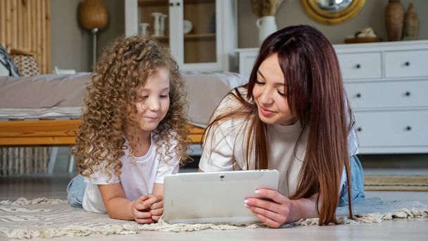 Brunette mom and kid girl play online game on white tablet - Foto, afbeelding