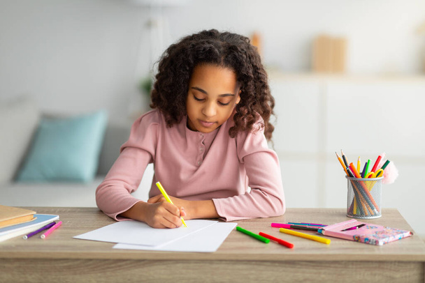 African american schoolgirl sitting at table and drawing, painting with pencils at home, enjoying development activities - Foto, Bild
