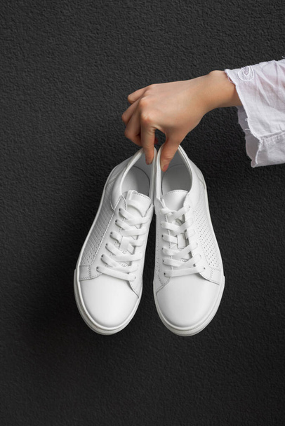 White sneakers in female hand at black background - Photo, image