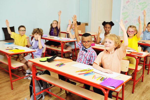 Small children school children smile and hold their hand up for a response against the background of a female teacher and a school class. Back to schoo - Φωτογραφία, εικόνα