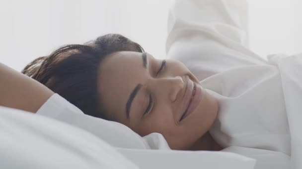 Jó reggelt és kényelmes alvást. Fiatal, kipihent afro-amerikai nő nyújtózkodik az ágyban és mosolyog a kamerába - Felvétel, videó