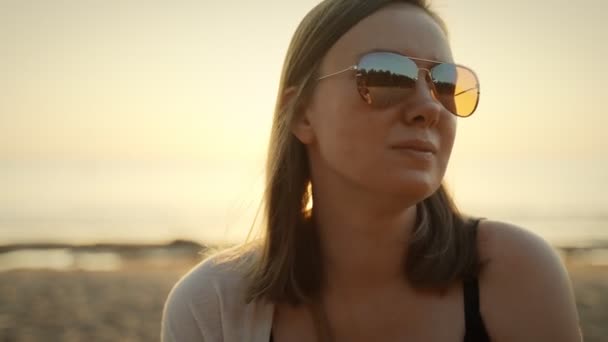 Portrét krásné ženy v slunečních brýlích u moře při západu slunce. - Záběry, video