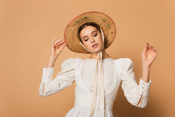 giovane donna in abito bianco regolazione cappello di paglia su beige  - Foto, immagini
