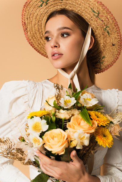 young woman in straw hat holding bouquet of flowers on beige - Fotoğraf, Görsel