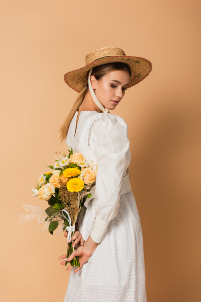ドレスの若い女性とベージュの後ろに花の花束を持っている麦藁帽子 - 写真・画像