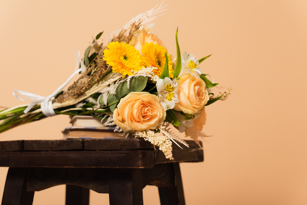 bukiet różnych kwiatów na książkach i drewniane krzesło izolowane na beżu  - Zdjęcie, obraz