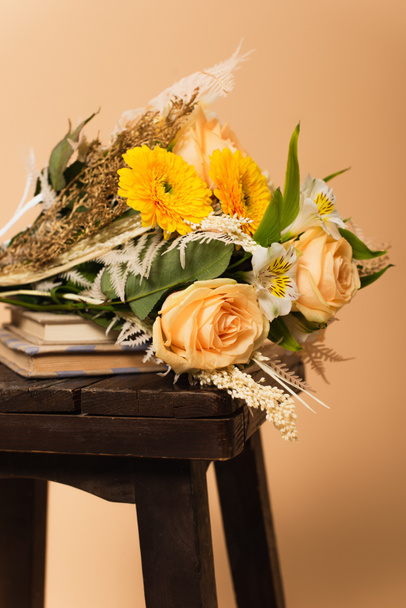 ramo de flores diferentes en libros y silla de madera aislada en beige  - Foto, Imagen