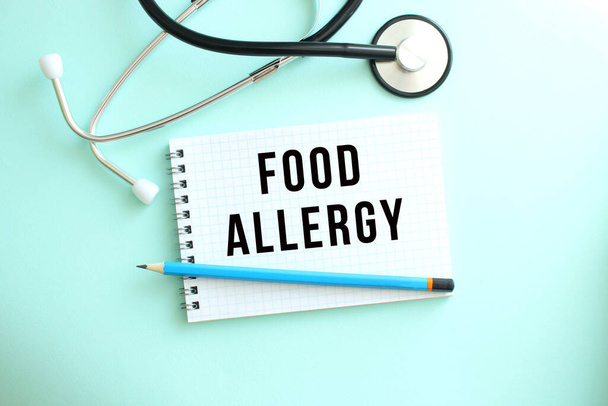 White notepad with the words FOOD ALLERGY and a stethoscope on a blue background. Medical concept - Foto, imagen