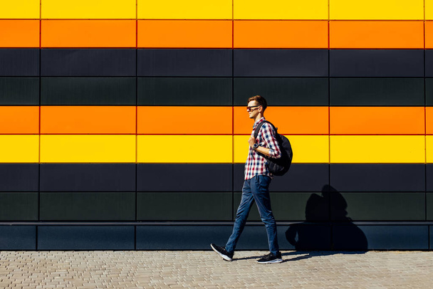 Full length, photo of a positive carefree joyful optimistic guy, wearing glasses and a shirt, with a briefcase, walking somewhere on an isolated multicolored bright background - Фото, изображение