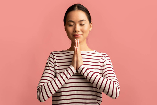 Портрет красивой молодой азиатки, молящейся с сжатыми руками у лица - Фото, изображение