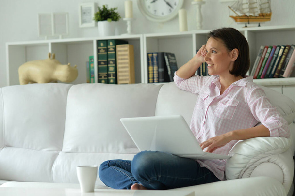 Young beautiful woman with laptop on sofa at home - Φωτογραφία, εικόνα