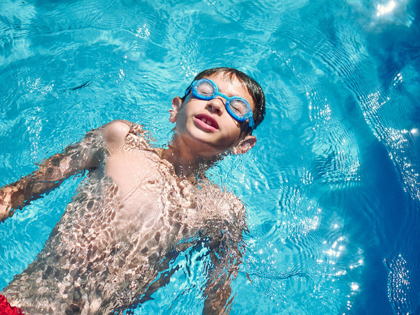 gros plan d'un garçon de 8 ans nageant sur une piscine, concept d'amusement d'été - Photo, image