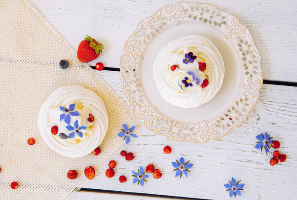 Small meringue cakes, decorated with whipped cream, fresh berries and real life edible flower blossoms. - Фото, изображение