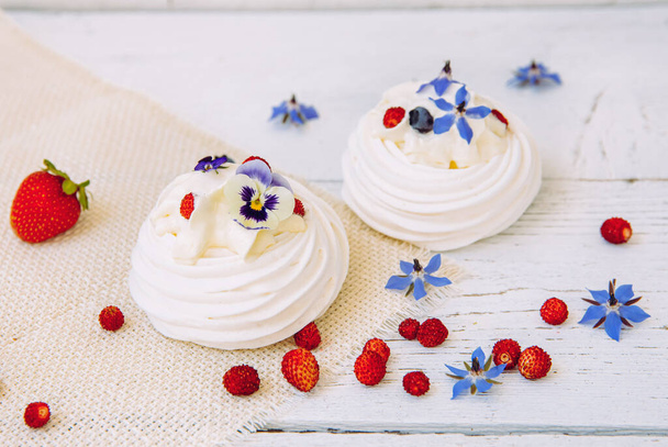Small meringue cakes, decorated with whipped cream, fresh berries and real life edible flower blossoms. - Photo, Image