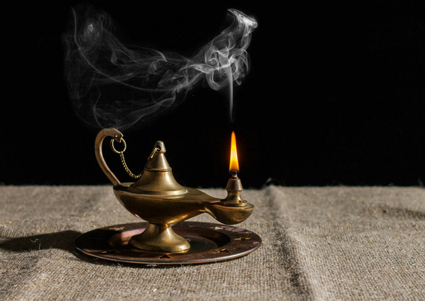 burning magic lamp of aladdin on table. indoor closeup on black background - Photo, Image