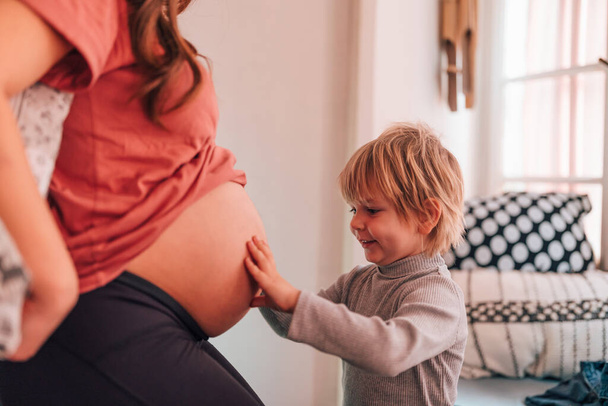 Ritratto di una donna incinta con un bambino che si abbraccia a casa. Famiglia persone amore concetto - Foto, immagini