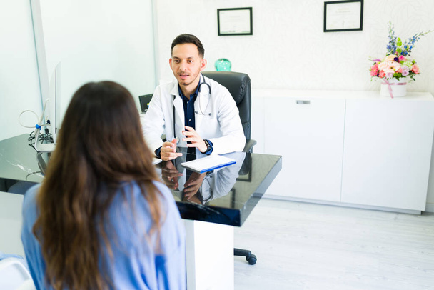 Giving a medical diagnosis. Male otolaryngologist doctor explaining a medical treatment to a female patient sitting at his office desk - Foto, Imagen