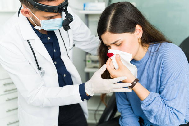 専門の耳鼻咽喉科医は、女性患者の鼻出血を停止しようとしています.医者の鼻血で苦しんでいるラテン語の女性 - 写真・画像