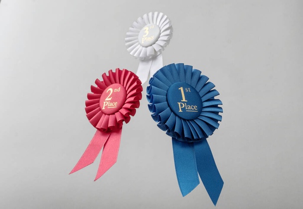 Drei Rosetten fliegen über grauen Hintergrund als Preise an Gewinner und Champions für Qualität und Sieg. - Foto, Bild