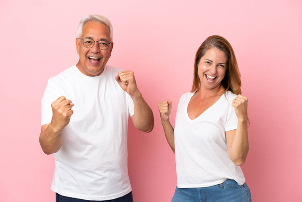 Middle age couple isolated on pink background celebrating a victory in winner position - Fotoğraf, Görsel