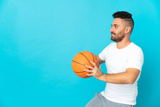 Caucásico hombre aislado en azul fondo jugando baloncesto - Foto, imagen