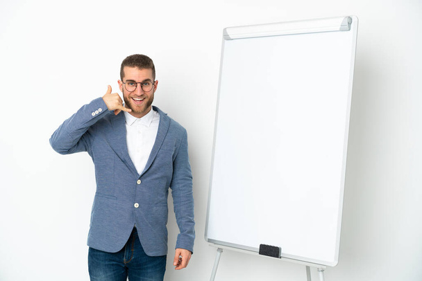 Jonge zakenvrouw geeft een presentatie op het witte bord geïsoleerd op witte achtergrond het maken van telefoon gebaar. Bel me terug. - Foto, afbeelding