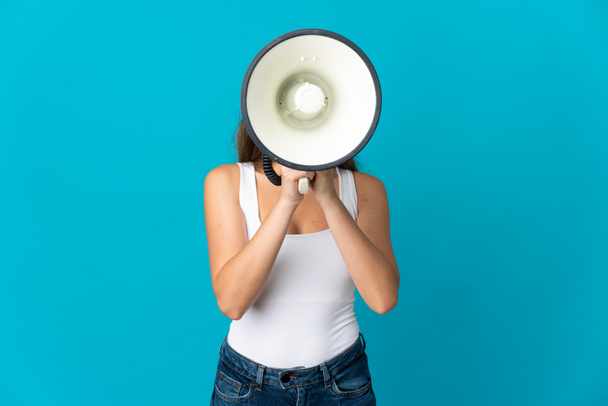 jonge blanke vrouw geïsoleerd op blauwe achtergrond schreeuwen door een megafoon om iets aan te kondigen - Foto, afbeelding