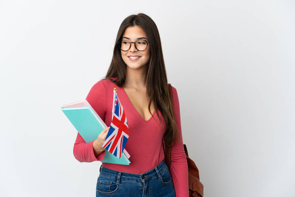 Adolescente brasileña sosteniendo una bandera del Reino Unido aislada sobre fondo blanco mirando hacia un lado y sonriendo - Foto, imagen