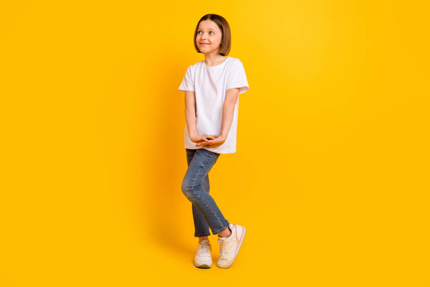 Full length body size photo schoolgirl in casual clothes smiling looking copyspace isolated vibrant yellow color background - 写真・画像