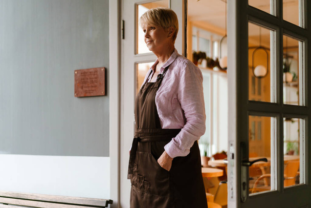 Mature woman wearing apron standing in cafe outdoors - Fotó, kép