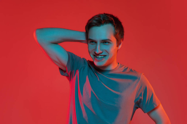 One young smiling handsome caucasian guy isolated on red neon background. Concept of human emotions, facial expression. - Foto, imagen