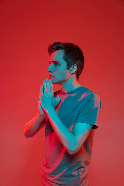 Vertikales Porträt eines jungen kaukasischen Mannes isoliert auf rotem Neon-Hintergrund. Konzept menschlicher Emotionen, Mimik. - Foto, Bild