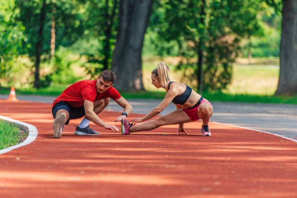 Jeune couple attrayant s'étirant ensemble sur un circuit après avoir fait de l'exercice à l'extérieur - Photo, image