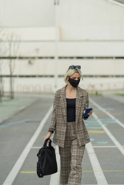 Geschäftsfrau geht und kaut ihr Handy, während sie ihre Maske trägt - Foto, Bild