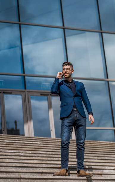 Бизнесмен-предприниматель разговаривает по телефону с офисными зданиями на заднем плане - Фото, изображение