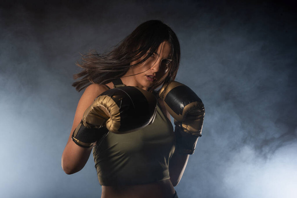 Retrato de close-up de uma boxeadora posando com luvas de boxe e olhando para a câmera com um fundo esfumaçado - Foto, Imagem