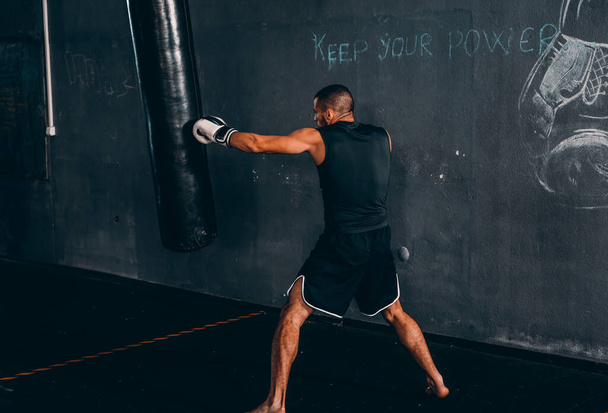 Boxertraining mit Boxsack in dunkler Sporthalle. Boxer als Übung für den großen Kampf. Boxer schlägt auf Boxsack ein - Foto, Bild