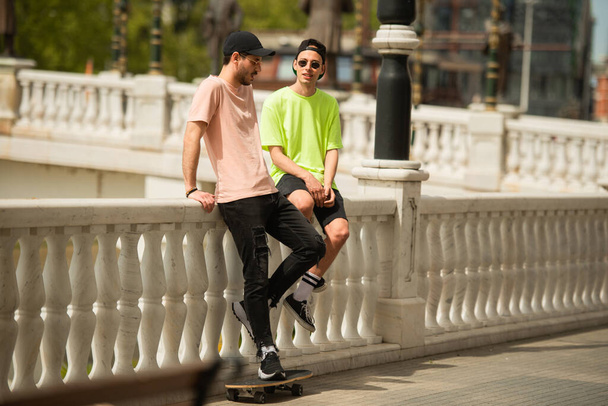Two male friends are talking while sitting on the bridge - Photo, Image