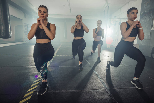 Grupa sportowców w odzieży sportowej ćwiczy longe na siłowni lewą nogą - Zdjęcie, obraz