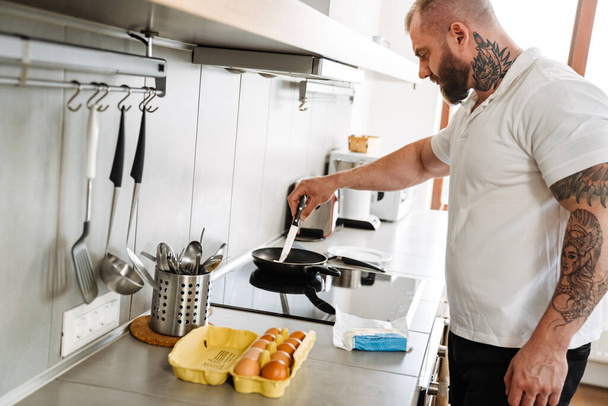 White man with beard cooking fried egg in kitchen at home - Photo, image