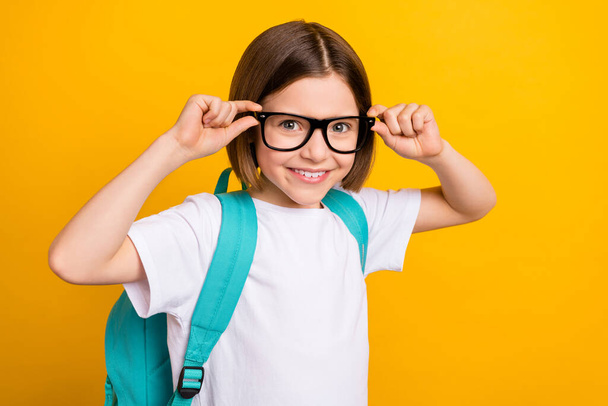 Photo portrait small schoolgirl smiling wearing glasses blue backpack isolated vivid yellow color background - Фото, зображення